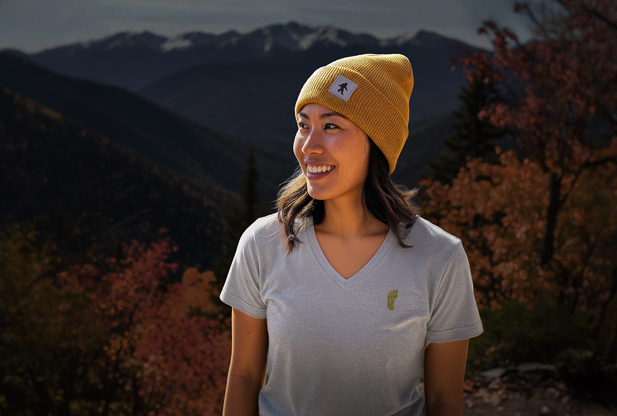 Woman in The Real Bigfoot v-neck and beanie with autumn mountains in background.